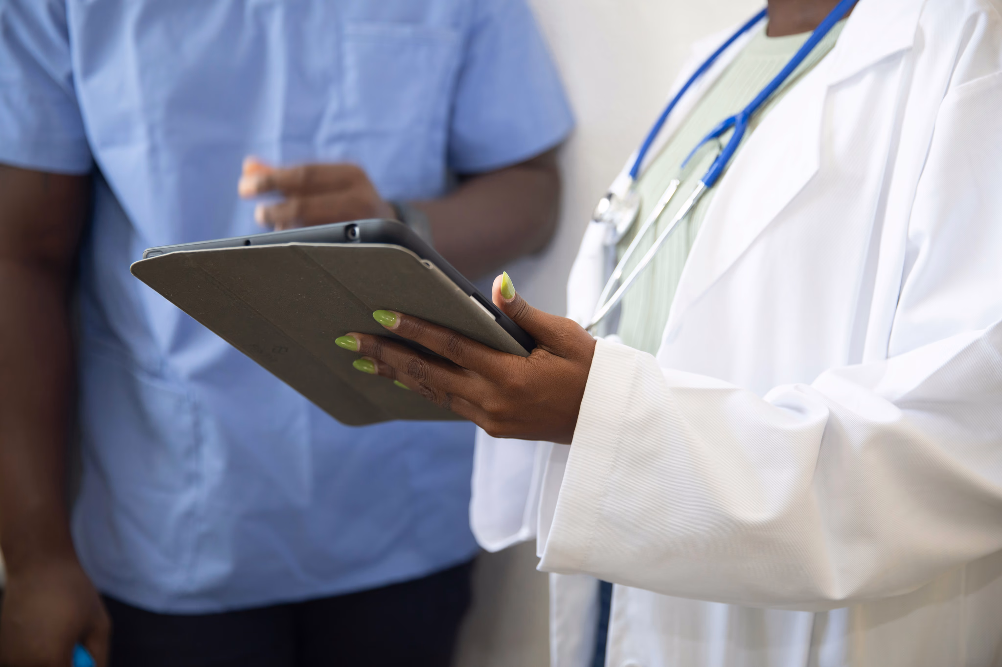 A physician in a white coat reviewing a patient chart on a tablet alongside a colleague.