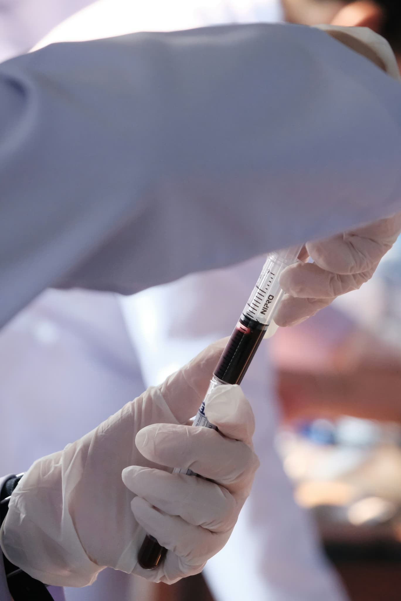 Manos con guantes sosteniendo un tubo de muestra de sangre